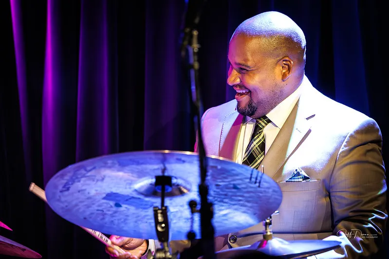 Sean laughing behind the ride cymbal in a cream suit. Photo: Jeff Dunn Jazz Photography.