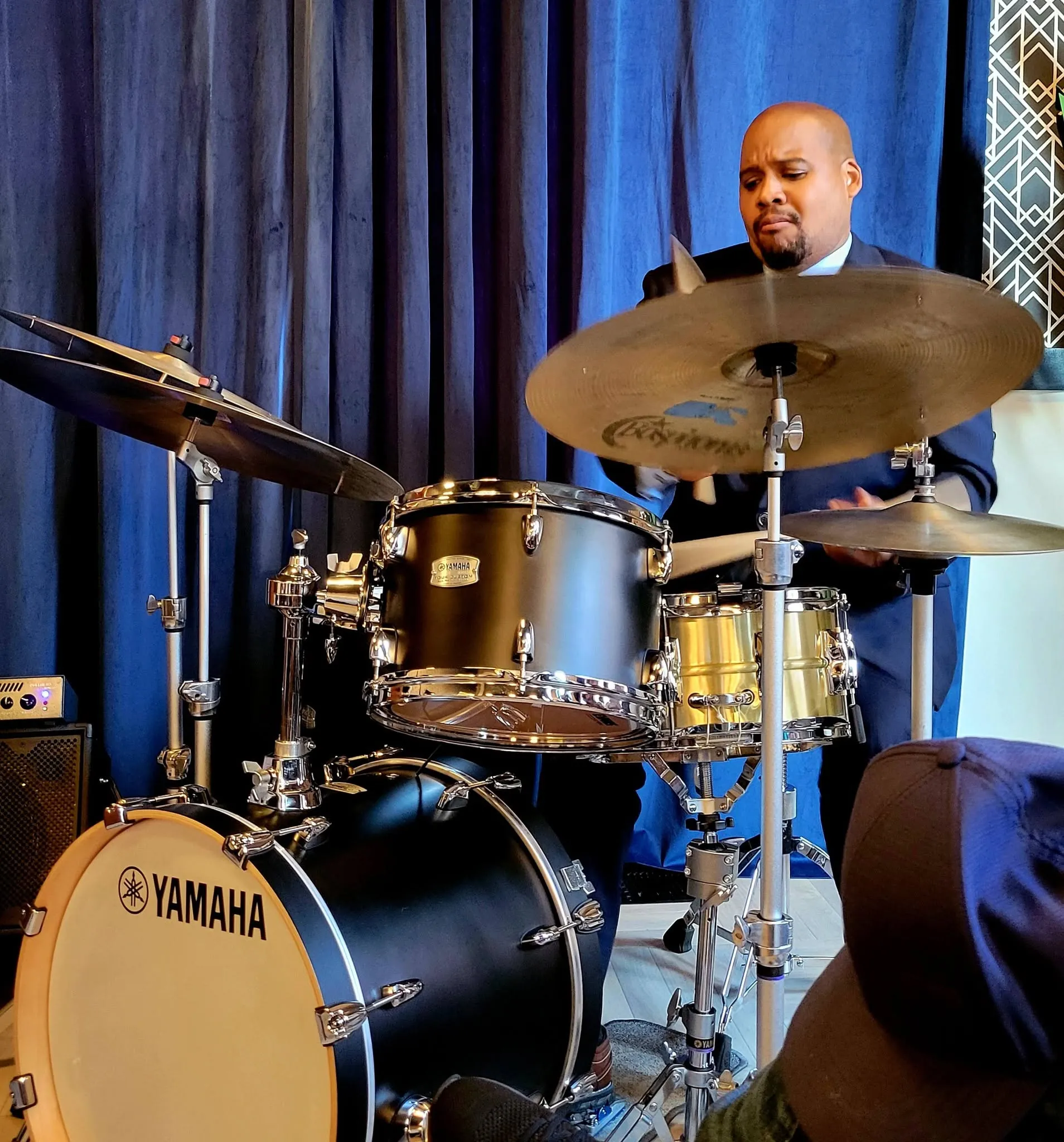 Sean at a Yamaha kit against blue curtains, mid-phrase.